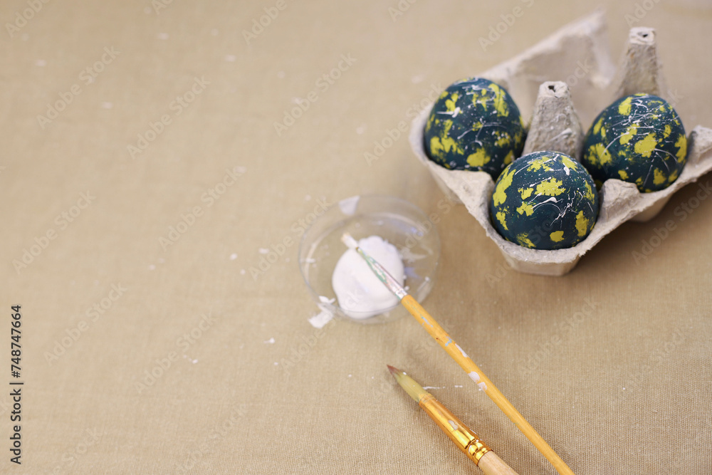 There are colored eggs in an egg tray for Easter. green eggs with yellow spots, white dots and lines. brushes and paint nearby There are colored eggs in an egg tray for Easter. green eggs with yellow spots, white dots and lines. brushes and paint nearby