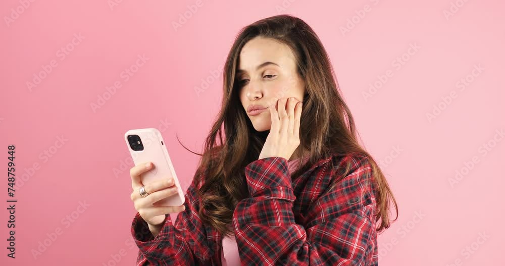Calm beautiful young woman isolated on pink background. Girl in pink pullover flirting while chatting on mobile phone, dreaming. Woman think about answer, touch lip, look at side, unsure. Calm beautiful young woman isolated on pink background. Girl in pink pullover flirting while chatting on mobile phone, dreaming. Woman think about answer, touch lip, look at side, unsure.