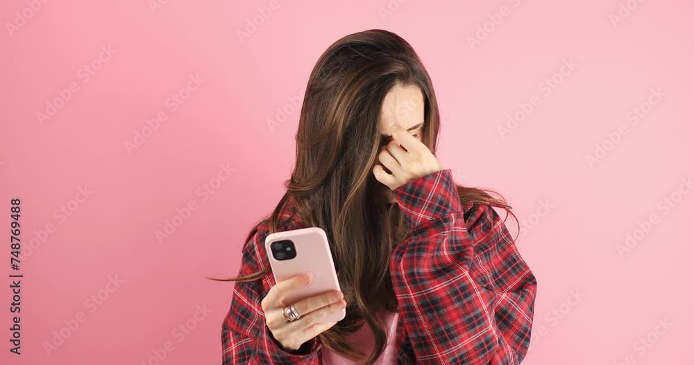 Exhausted young woman hurt eye while using mobile phone. Attractive girl feeling visual fatigue and eye strain tired from overwork and massage dry irritable eye standing isolated pink background. Exhausted young woman hurt eye while using mobile phone. Attractive girl feeling visual fatigue and eye strain tired from overwork and massage dry irritable eye standing isolated pink background.