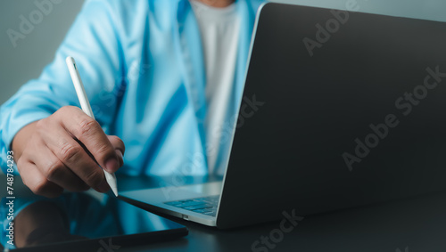 Businessman in black suit working on laptop computer and tablet, Hand touch on tablet at office with dark background, Online working, Close up, Copy space.