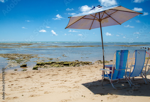 beach chairs and umbrella on the beach in summer day with blue sky, corals and natural pool