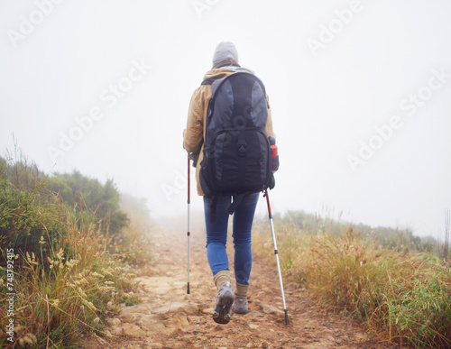 Person, hiking and back in nature with trekking sticks, winter and support for fog trail in mountain. Athlete, backpack and sport gear for safety in wet environment, slippery and walking for fitness