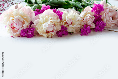 Horizontal frame with a bright and delicate bouquet of peonies with field carnations in the form of a frame according to a pattern on a white wooden background.