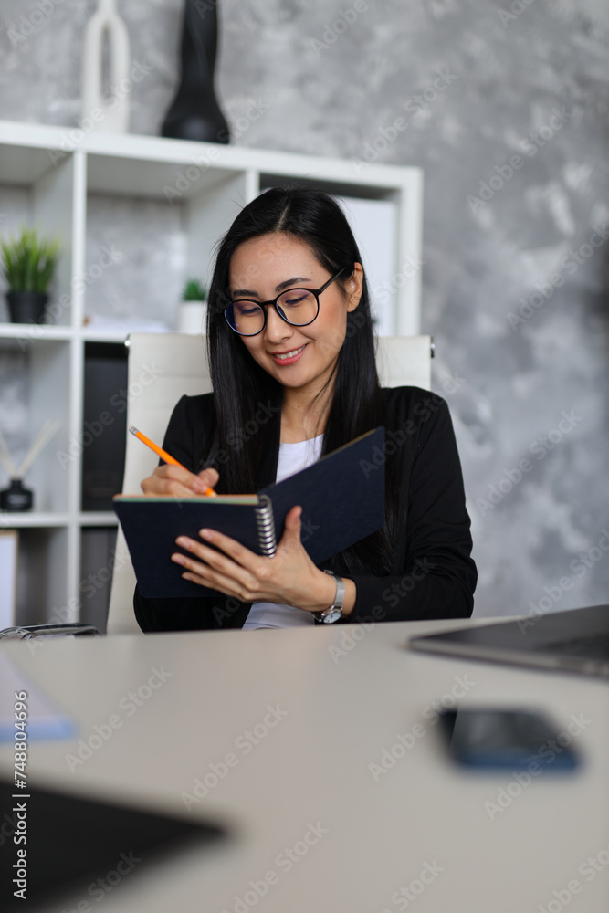 A young Asian businesswoman in a modern office, confidently posing with a tablet, portraying success.
