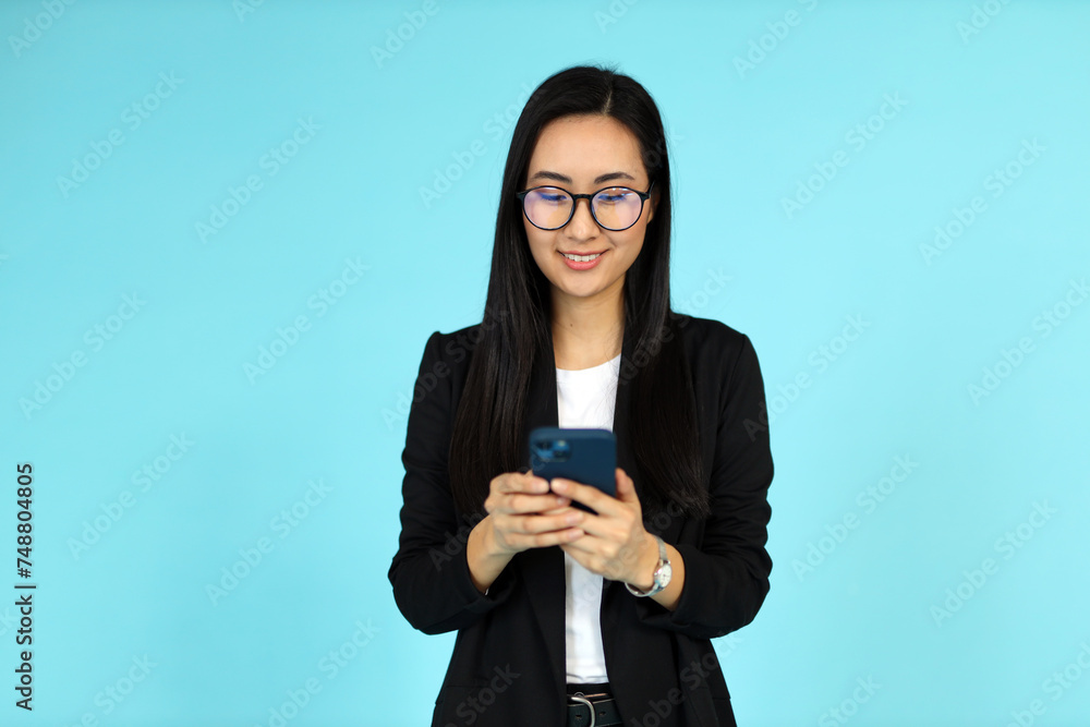 A young Asian woman holds a smartphone, portraying beauty and professionalism against a blue background. A young Asian woman holds a smartphone, portraying beauty and professionalism against a blue background.
