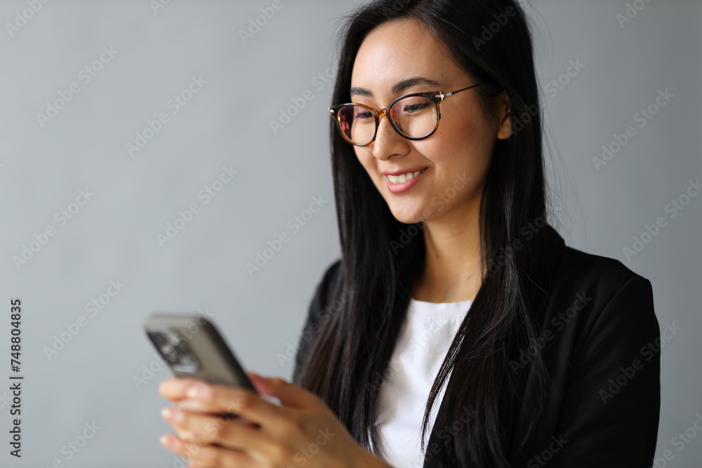 A young Asian woman happily uses her smartphone, embodying modern communication and technology. A young Asian woman happily uses her smartphone, embodying modern communication and technology.