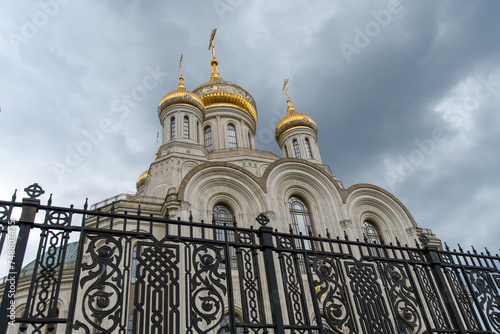 The golden domes of an Orthodox church behind a forged figured fence against the blue sky.