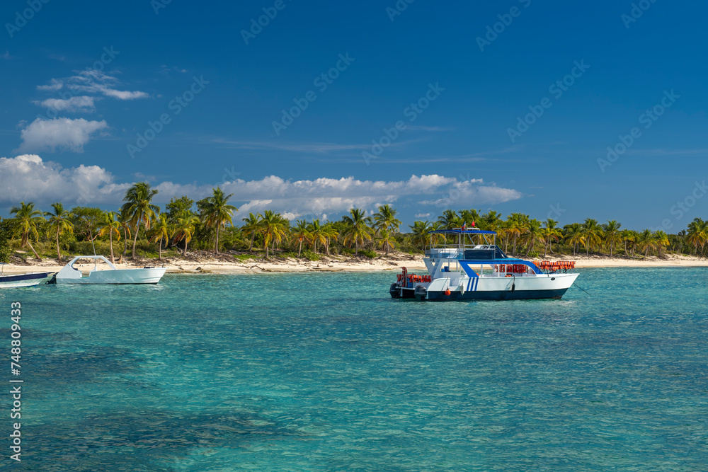 Seascape with crystal clear shallow turquoise ocean water, deep blue sky and tour boat with white sand secluded pristine beach in the background. Catalina Island, Dominican Republic. Wide angle shot.