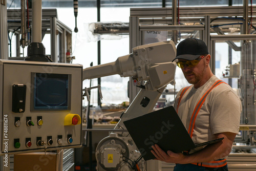 engineer in white t-shirt programming robot on assembly line using laptop blurred background
