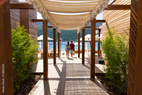 A couple walks on a wooden deck through a beach cafe to the Adriatic Sea. Montenegro, Tivat.