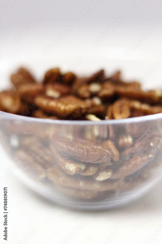 Obraz premium Pecan halves in glass bowl. Isolated on white background.