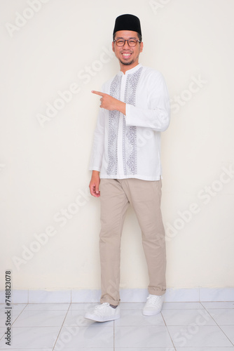 Full body portrait of moslem man smiling and pointing to the the right side