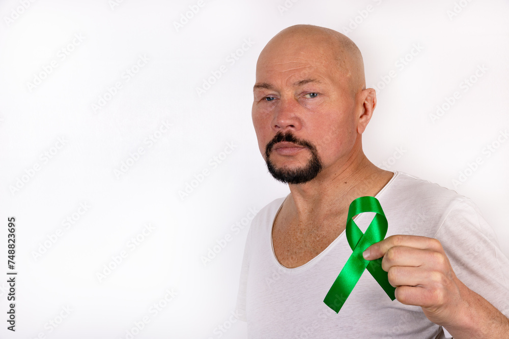 A man holds a green ribbon on the background of his t-shirt. Medical kidney cancer awareness concept. A man holds a green ribbon on the background of his t-shirt. Medical kidney cancer awareness concept.