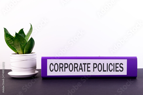 Folder with the text label Corporate Policies lies on a dark table with a flower and a light background.