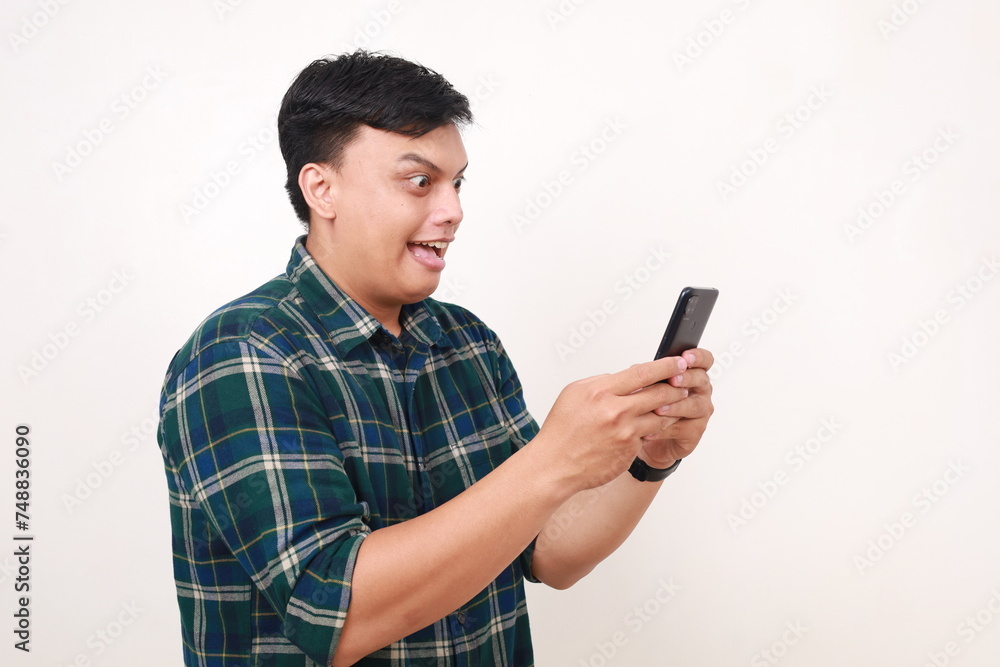 Side view of surprised young asian man while getting a news from his phone Side view of surprised young asian man while getting a news from his phone