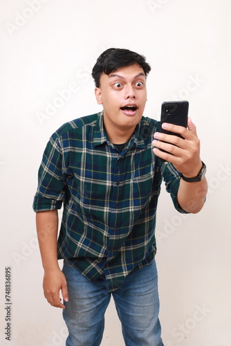 Shocked young asian man with open mouth and wide eyes while receiving a news from his phone