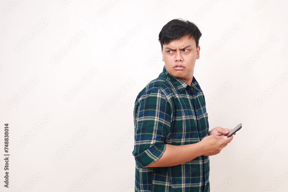 Side view of Curious young asian man holding a cell phone while looking behind Side view of Curious young asian man holding a cell phone while looking behind