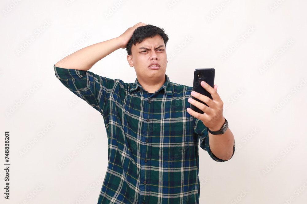 Unhappy young asian man touching his head while holding a cell phone Unhappy young asian man touching his head while holding a cell phone