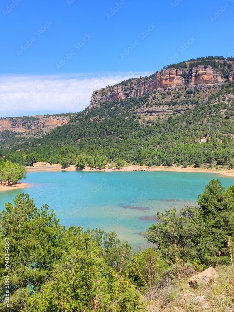 Lake with turquoise water between mountains and trees on a sunny day with blue sky
