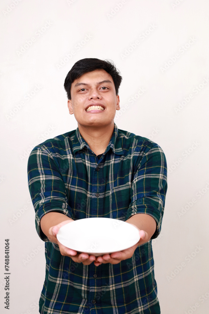 Young asian man showing happy expression while holding an empty plate Young asian man showing happy expression while holding an empty plate