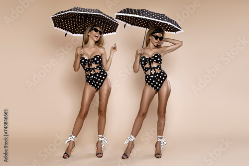 Beautiful young happy woman with blonde hair and a slim figure is posing in a polka-dot bikini and holding a polka-dot umbrella. Pin-up style girl