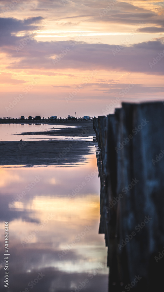 Lever du soleil et reflet dans l'eau de mer sur une plage en camargue avec des pêcheurs au loin et des poteaux en bois
