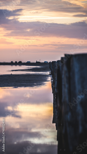 Lever du soleil et reflet dans l'eau de mer sur une plage en camargue avec des pêcheurs au loin et des poteaux en bois