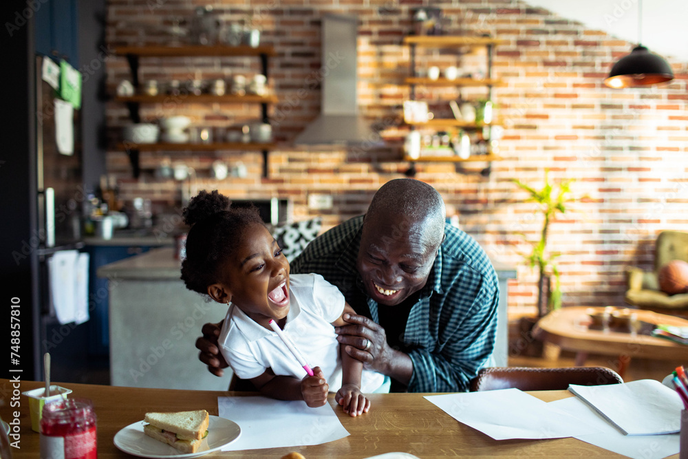 Grandfather laughing with granddaughter while doing homework in kitchen - obrazy, fototapety, plakaty 