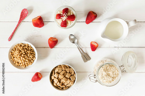 Bowls of whole meal oat cushions and oatmeal flakes, glass of porridge, strawberries and a milk jug