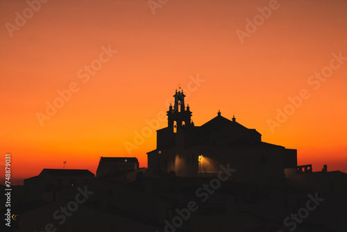 Iglesia católica de Nuestra Señora de las Flores en Sanlúcar de Guadiana, Huelva, España. Silueta del campanario de la iglesia en un cielo anaranjado durante la puesta de sol.
