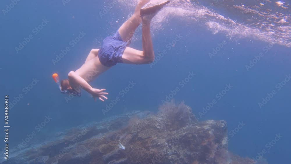 a noob newbie white Caucasian teen male boy wearing snorkel mask and fin duck free diving kicking down into the deep blue ocean water to beautiful pink red gorgonian sea fan and finger leather corals a noob newbie white Caucasian teen male boy wearing snorkel mask and fin duck free diving kicking down into the deep blue ocean water to beautiful pink red gorgonian sea fan and finger leather corals