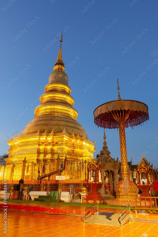 Naklejka premium Golden Buddhist stupa at Wat Phrathat Haripunchai Woramahawihan, Lamphun, Thailand, at dusk.