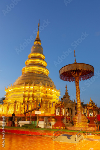 Wat Phrathat Haripunchai Woramahawihan. Golden buddhist stupa at dusk. © Eugene Ga