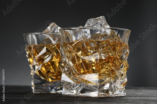 Whiskey and ice cubes in glasses on black wooden table, closeup
