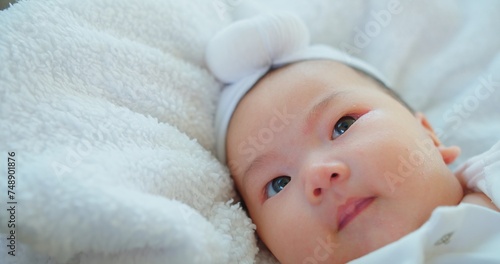 A contented baby with sparkling eyes and a soft headband lies on a plush fluffy white blanket, exuding warmth innocence and comfort