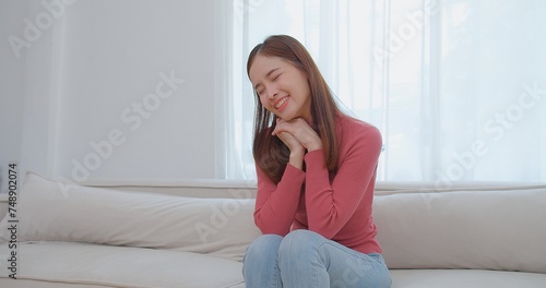 Ecstatic young asian woman in pink turtleneck holding looking at a pregnancy test and surprise exciting reaction laughing smile with happiness on a white couch, celebrating good news, a moment of joy