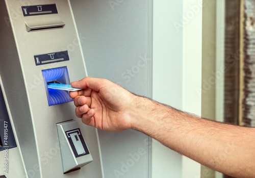 Young man put his credit card at the ATM on a city street.