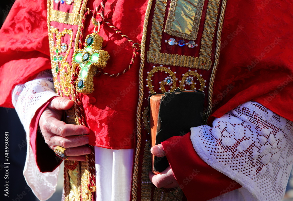 priest with red robe holding bible in hand during religious ceremony