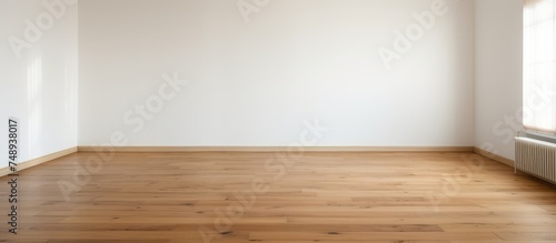 A room with laminate flooring and a white wall contains only a radiator and a window. The room appears bare and unoccupied, with a simple and minimalistic design.