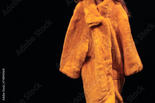 Bright yellow women's fur coat on a black background. Winter fashionable look