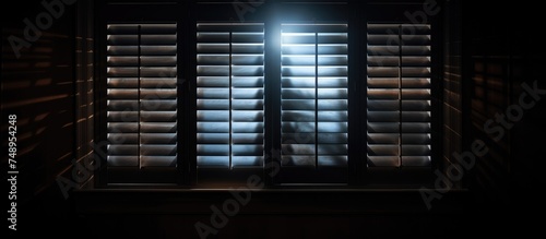 A dark room with shutters open and a beam of light shining through, illuminating the surrounding space with a soft glow. The light casts shadows and creates a contrast between brightness and darkness.