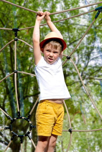 A child climbs up an alpine grid in a park on a playground on a hot summer day