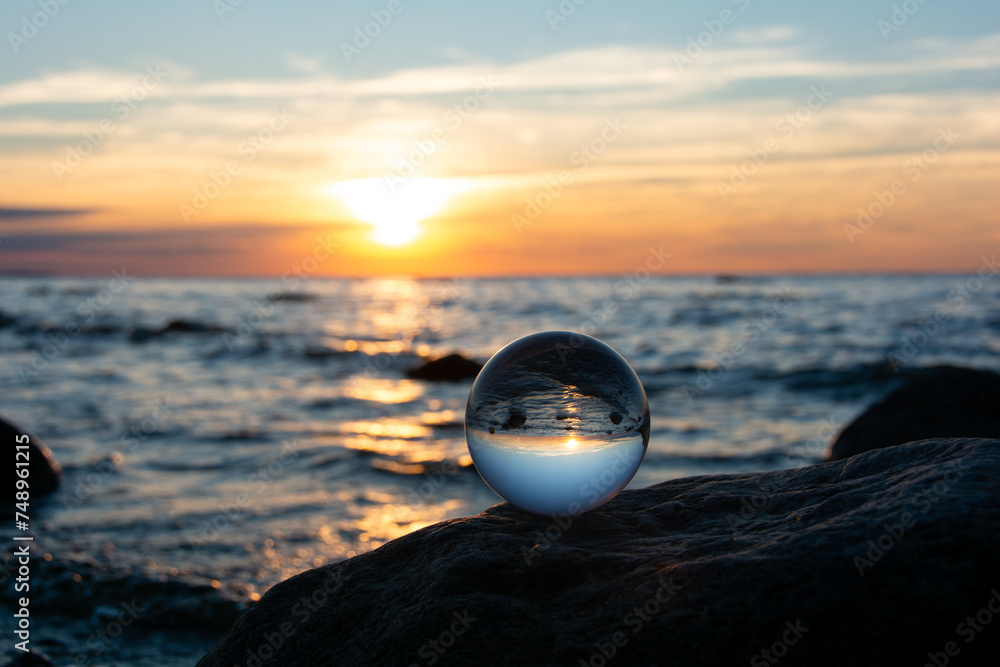 Ball made of glass lies on a stone in which the beach and the sea are ...