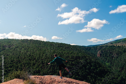 In a pine forest, a figure dressed in green attire dances, jumps with agility, demonstrates remarkable balance, and engages in light-hearted antics atop a rocky perch.