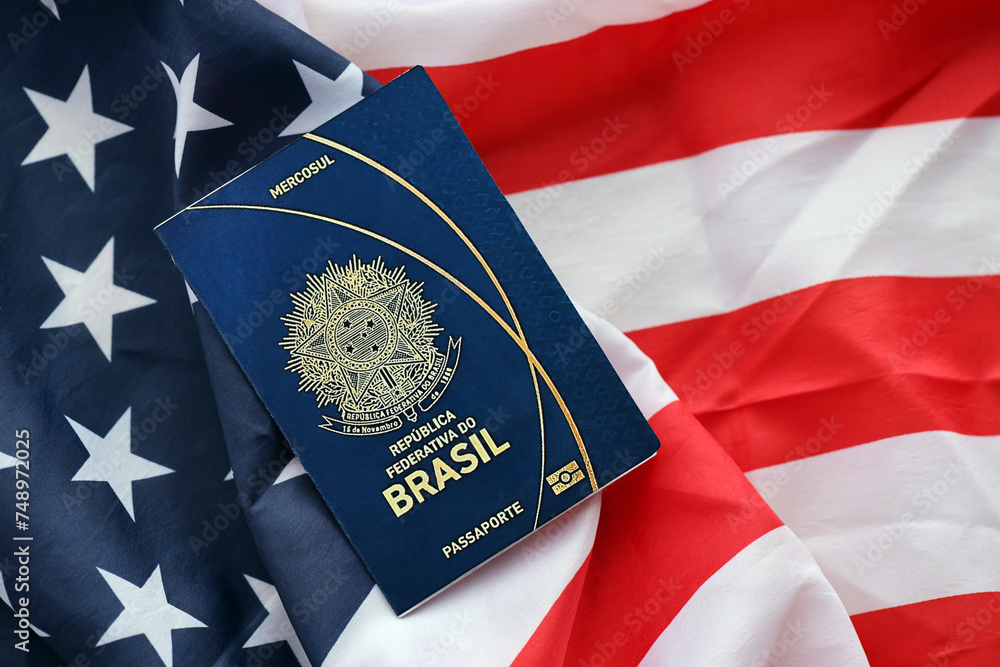 Naklejka premium Blue Brazilian passport on United States national flag background close up. Tourism and diplomacy concept