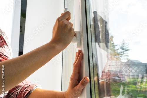 The hand holds the handle of a plastic double-glazed window, closing and opening the window with a rotary mechanism, the position of the handle for ventilation, micro-ventilation © Ольга Симонова