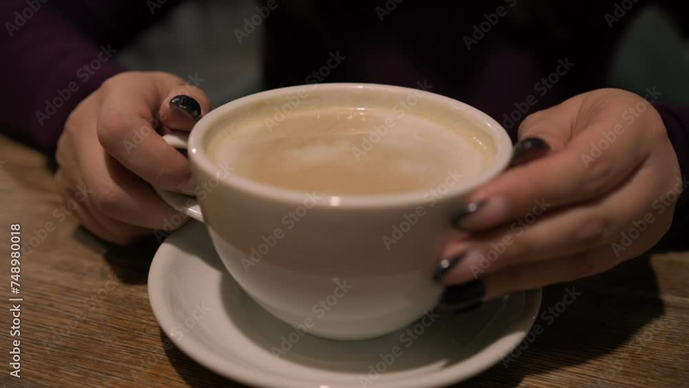 A woman is seated at a table, holding a cup of coffee in the cafe. A woman is seated at a table, holding a cup of coffee in the cafe.