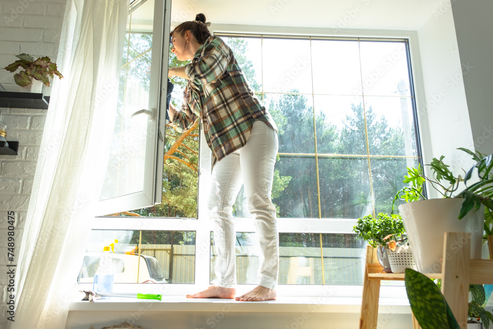 Woman manually washes the window of the house with a rag with spray cleaner and mop inside the interior with white curtains. Restoring order and cleanliness in the spring, cleaning servise