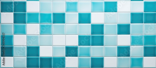 A wall covered in aqua and white ceramic tiles arranged in a grid pattern, creating a geometric mosaic texture. The squares on the wall are uniform in size and color, providing a simple yet visually