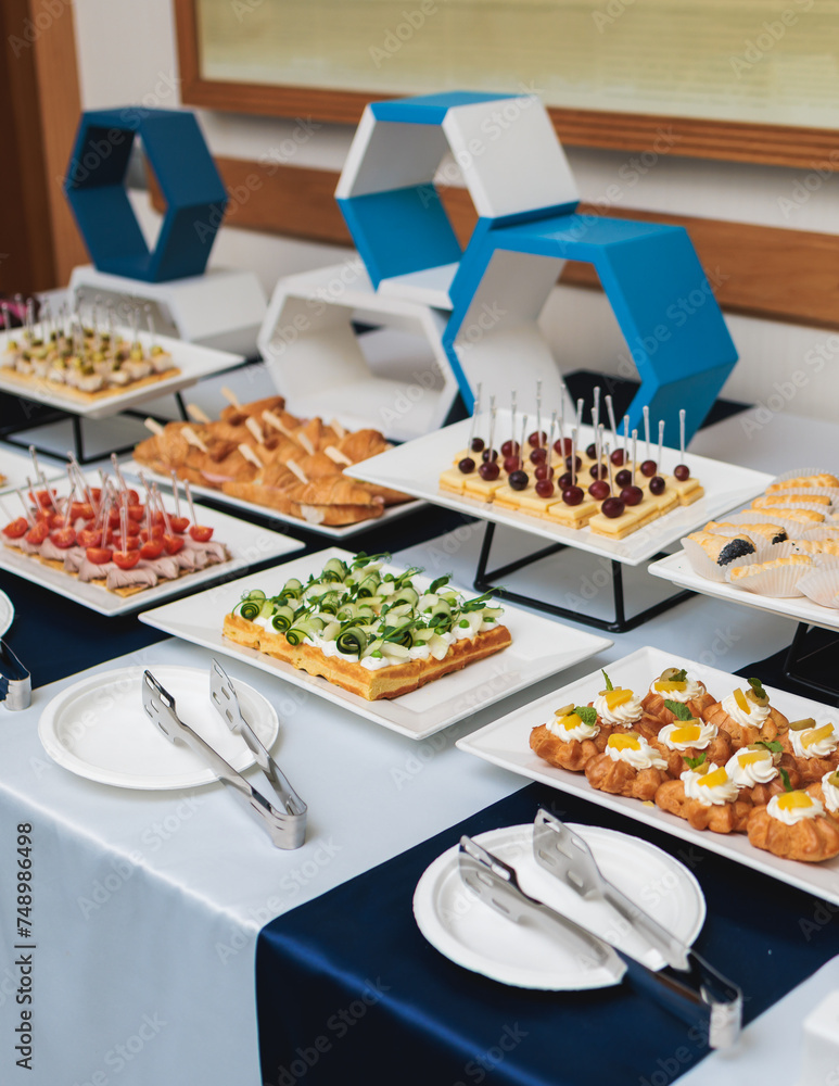 Beautifully decorated banquet catering table, with variety of with different food snacks appetizers on corporate birthday party event or wedding celebration, canape, salad, delicatessen setting